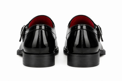 A pair of black patent leather double-strap loafers shown from the back, featuring a glossy finish, black soles, and a vibrant red interior lining, set against a plain white background.