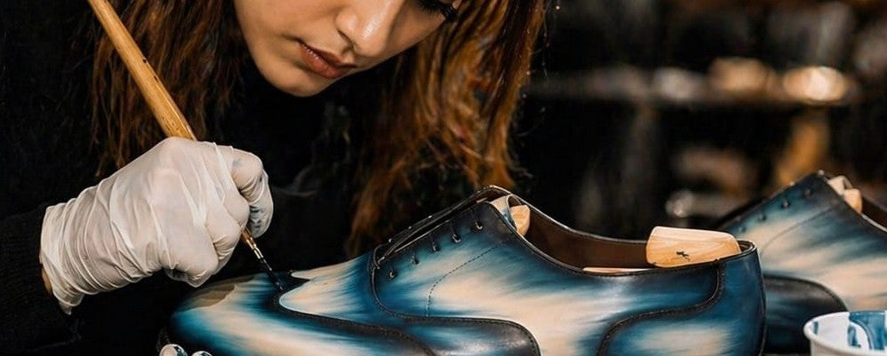 Person painting a shoe with blue and black design in a workshop setting